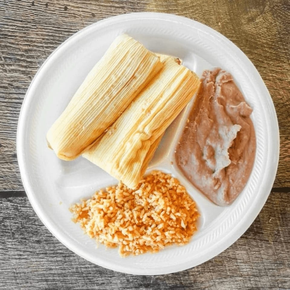 Two tamales, refried beans, and rice on a white plate from Antonio's Quick Lunch.