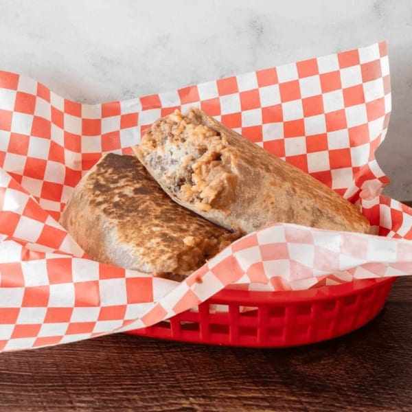 Two Antonio's Quick Lunch burritos, one cut open, in a red basket with checkered paper.