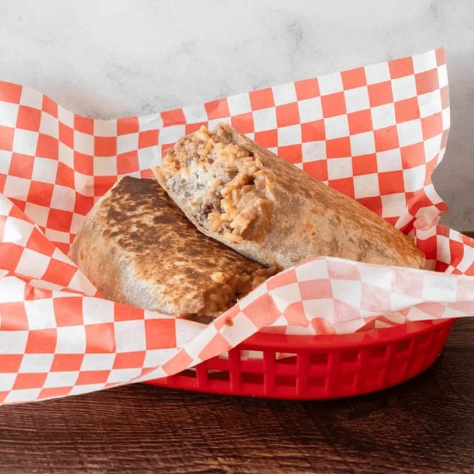 Two Antonio's Quick Lunch burritos, one cut open, in a red basket with checkered paper.