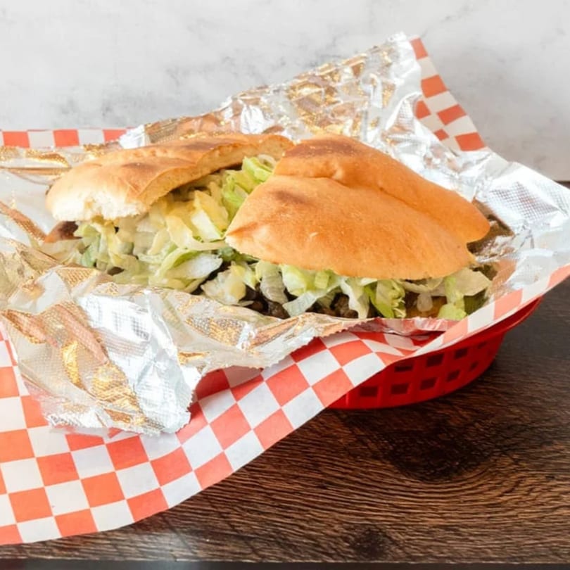 A Mexican torta sandwich with meat and shredded lettuce, served in a red basket with checkered paper.