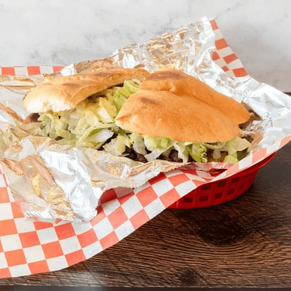 A Mexican torta with meat and shredded lettuce, served in a red basket lined with foil.