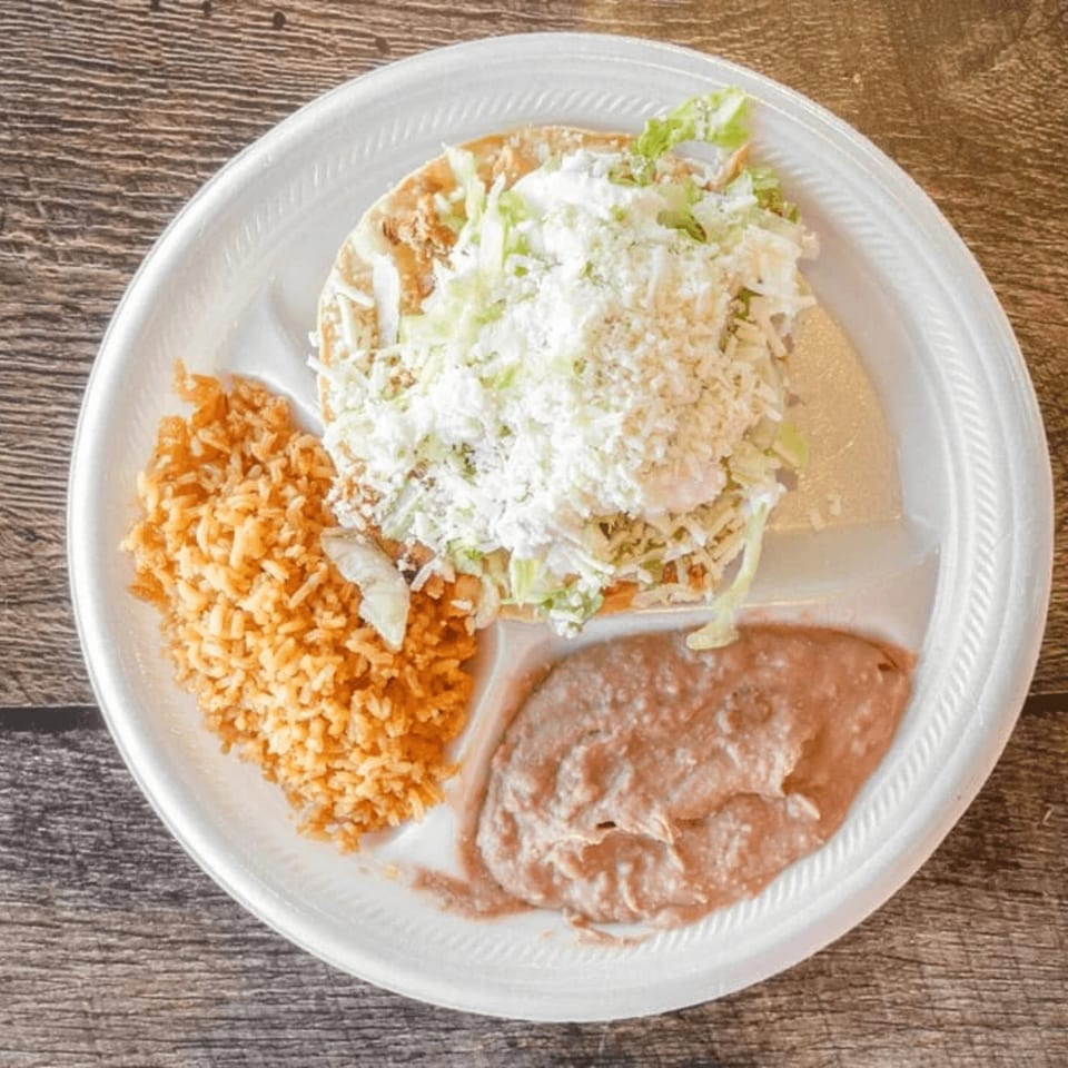 A Mexican tostada with rice and refried beans on a white partitioned plate.