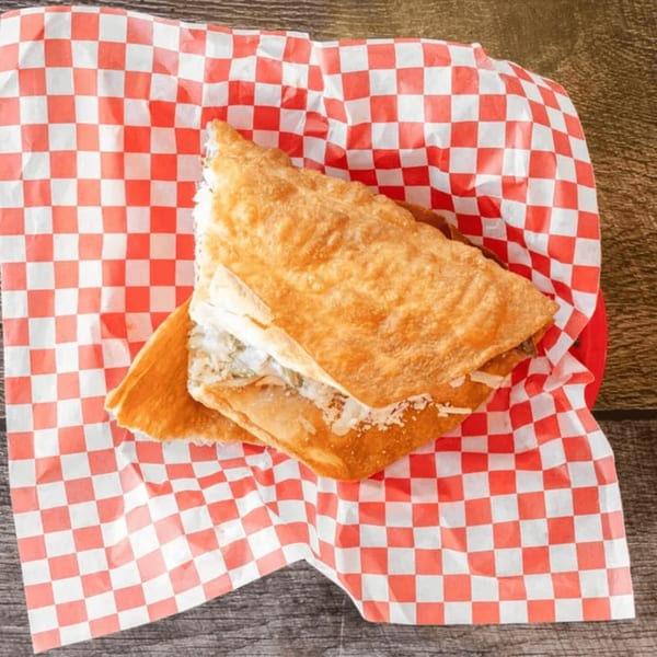 A golden-brown fried quesadilla, filled with cheese and meat, rests on red and white checkered paper.