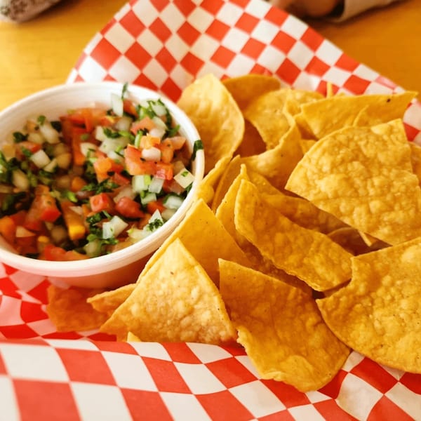 A white bowl of fresh pico de gallo with tortilla chips on red and white checkered paper.